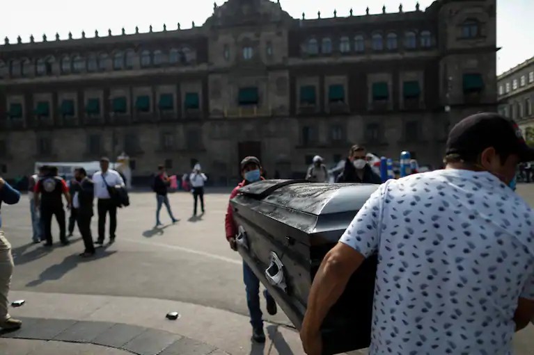 Dos hombres cargan un ataúd frente al Palacio Nacional, en Ciudad de México, al finalizar una protesta el 11 de mayo de 2020, en la que activistas de derechos humanos buscaron llamar atención a los riesgos de salud que enfrentan las personas en cárceles mexicanas esperando juicios que quedaron estancados por la pandemia por coronairus. (Rebecca Blackwell)